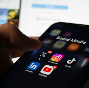 a-person-holding-a-smart-phone-with-social-media-on-the-screen.jpg A person holding a smart phone with social media on the screen